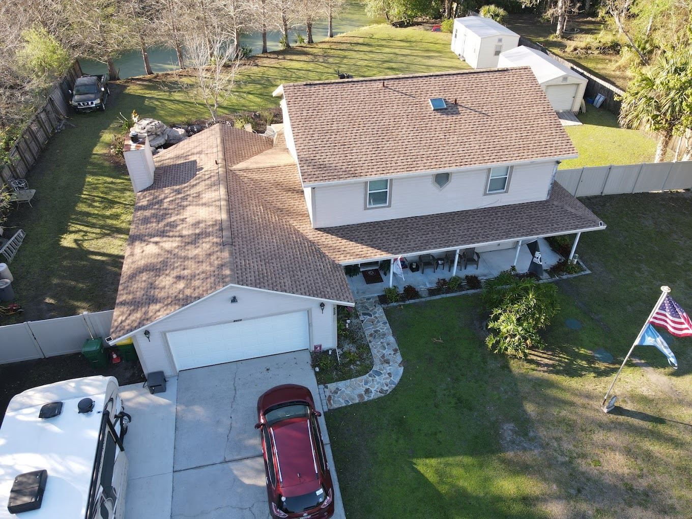 Aerial view of a two-story home with a brown roof, attached garage, stone walkway, and a red car parked in the driveway.