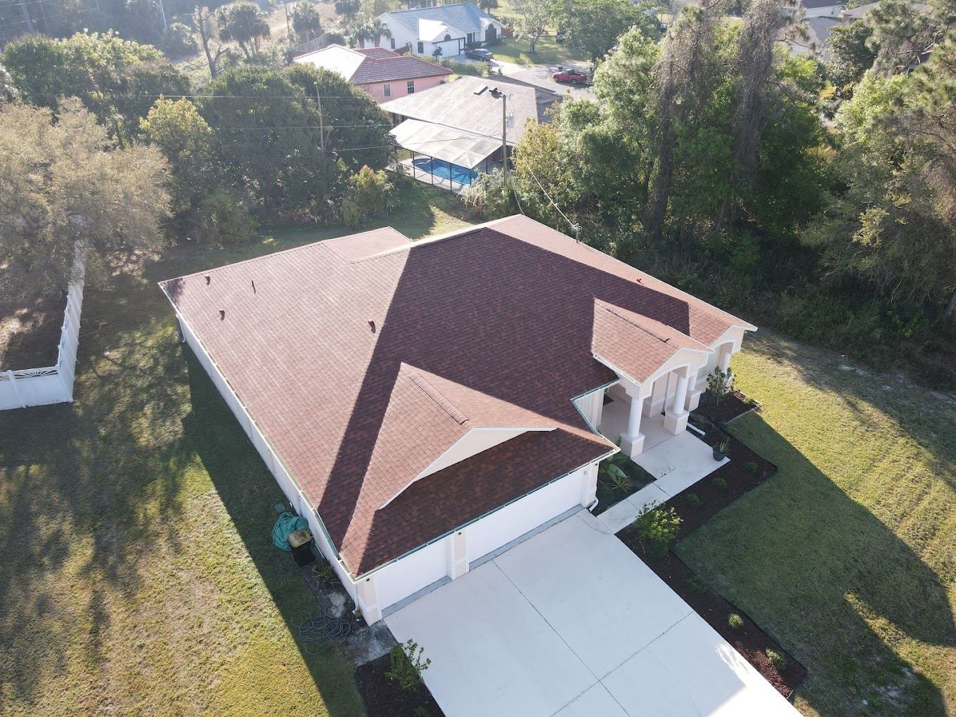 Aerial view of a residential home with a brown shingled roof, white garage doors, and a concrete driveway.