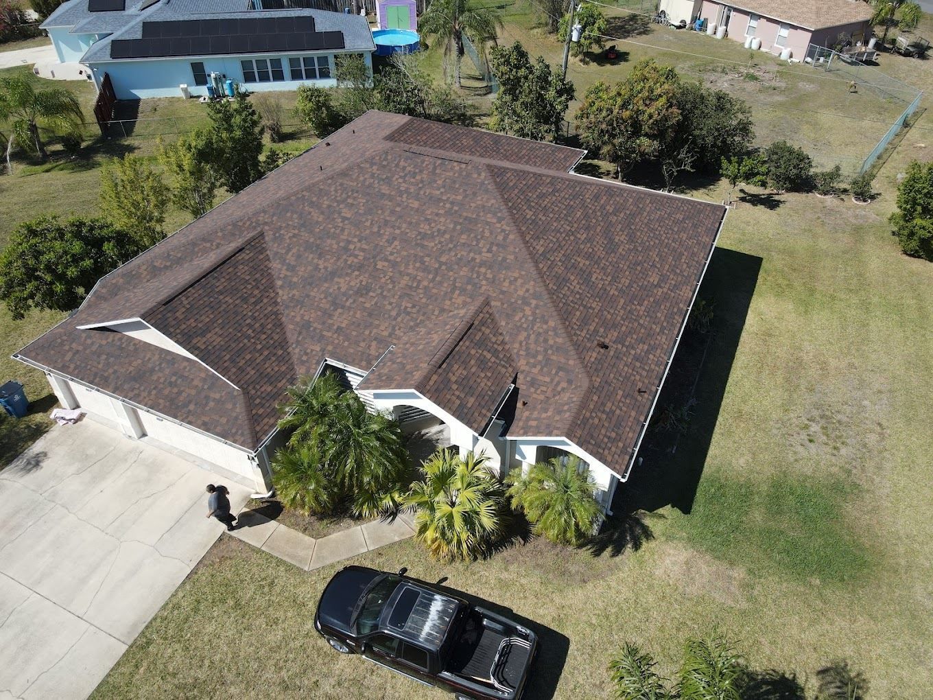 Aerial view of a residential home with a brown shingled roof, a front driveway, and a black pickup truck parked in front.