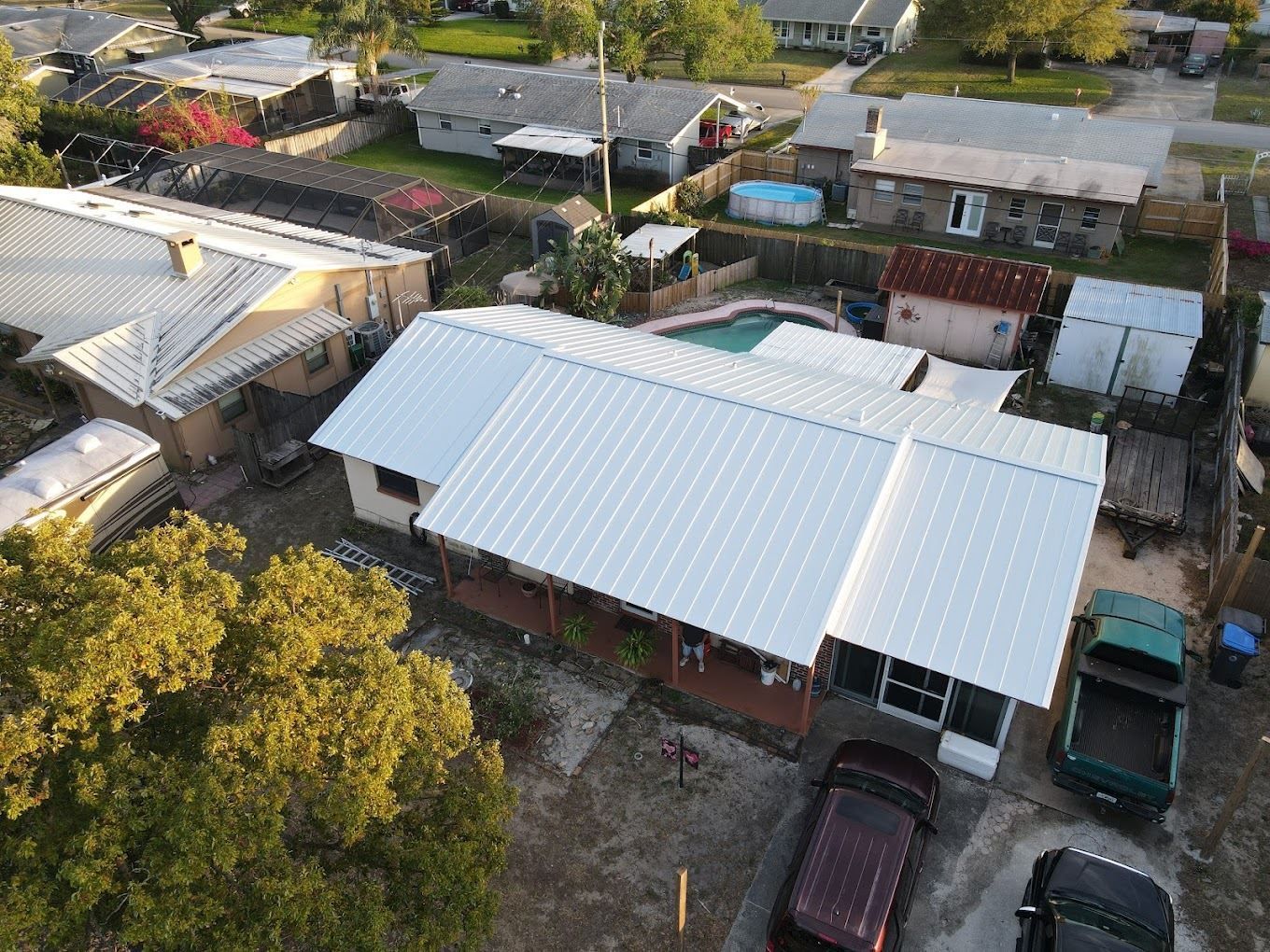 An aerial view shows a suburban neighborhood featuring a single-story house with a prominent white metal roof.