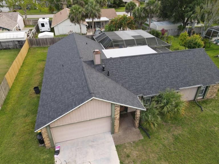 High-angle view of a single-story suburban house with a gray shingled roof, a garage, and a backyard pool enclosure.