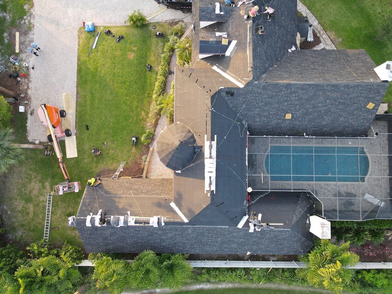 Aerial view of a residential roof replacement in progress, featuring workers, ladders, and a swimming pool in the yard.