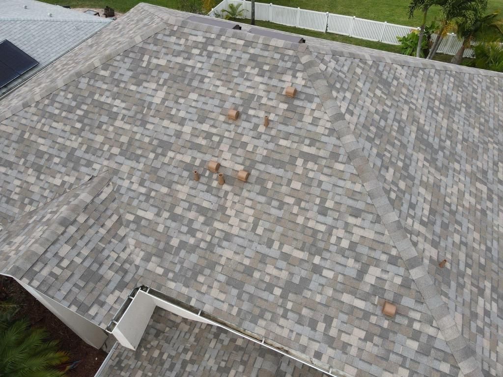 An aerial view of a multi-sloped residential roof covered in variegated grey and tan asphalt shingles.