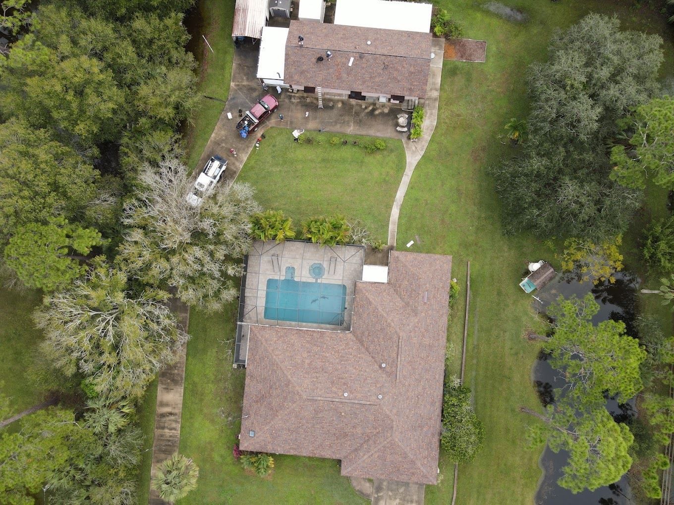 An aerial view of a property featuring a house with a pool, a separate detached garage, and surrounding green landscape.