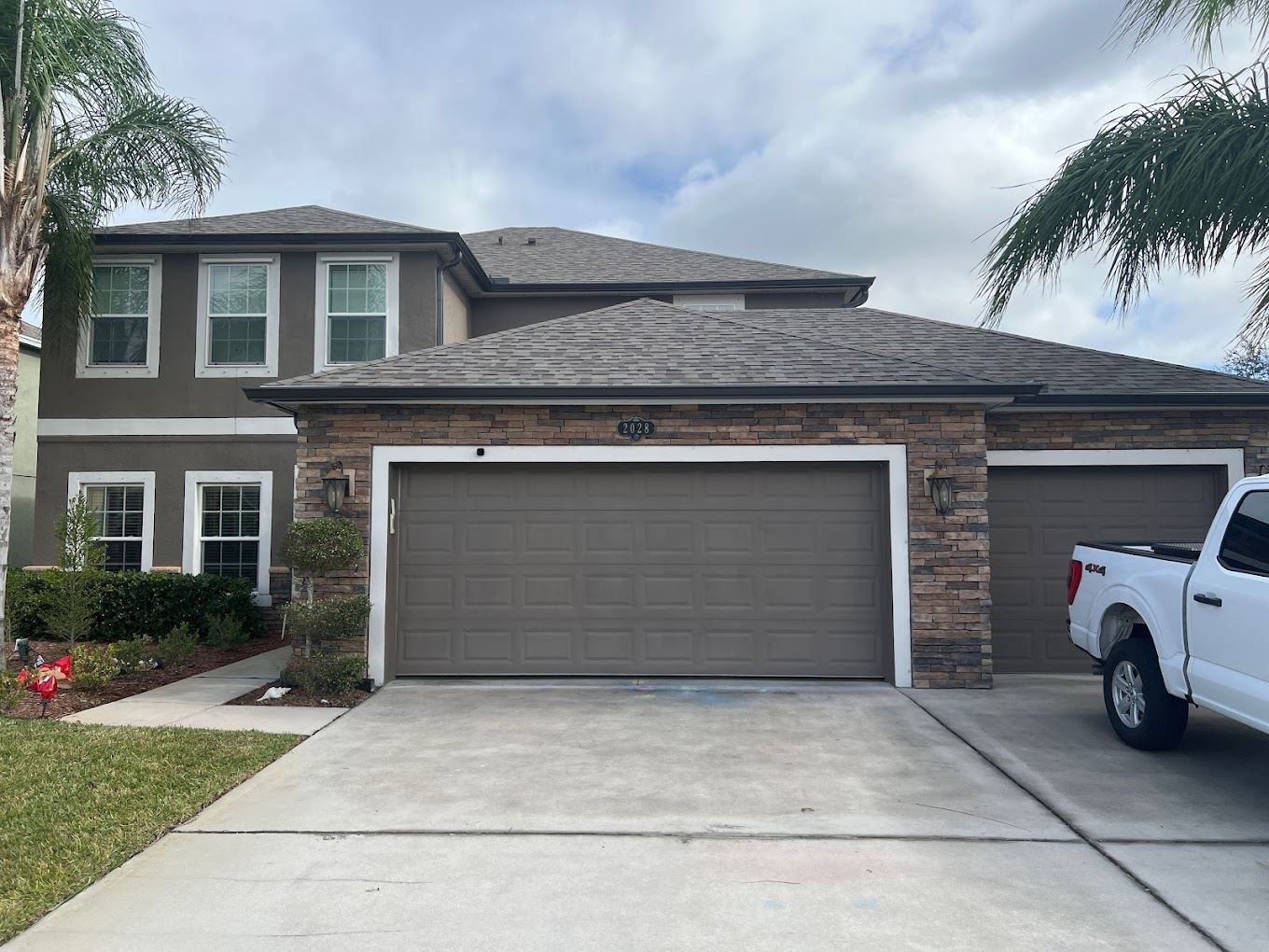 A two-story suburban home with a stone-accented facade, a three-car garage, and a white pickup truck in the driveway.