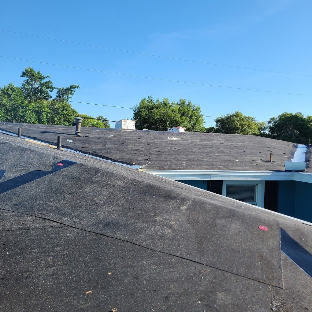 A low-angle view of a flat black roof with several vents and a white trim against a clear blue sky.