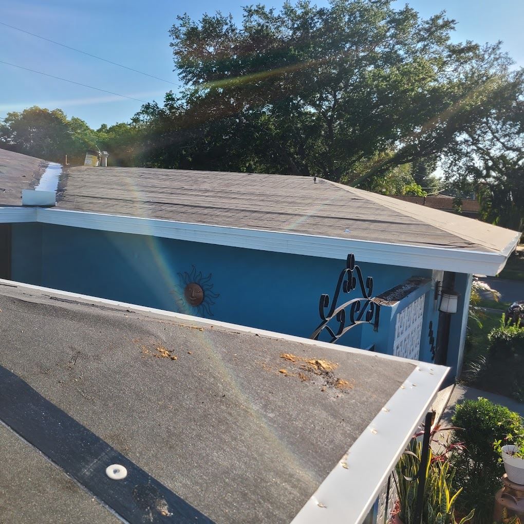 A high-angle view of two intersecting residential roof sections, one covered in asphalt shingles and one in flat roofing.