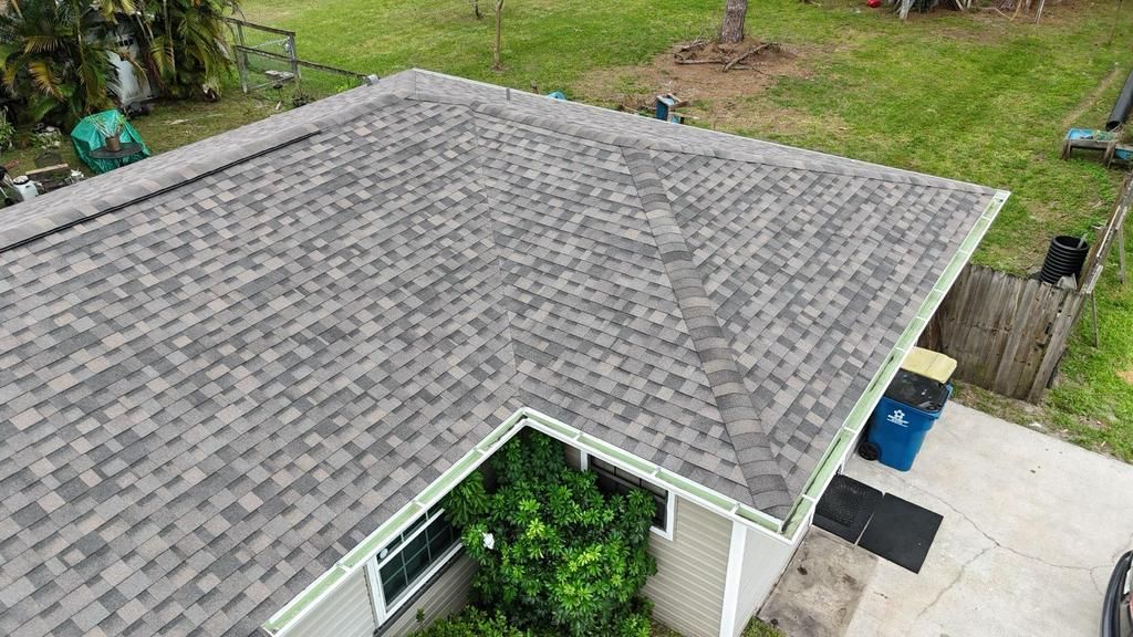 A high-angle view of a gray, textured shingle roof on a home, featuring a hip roof design and white gutters.