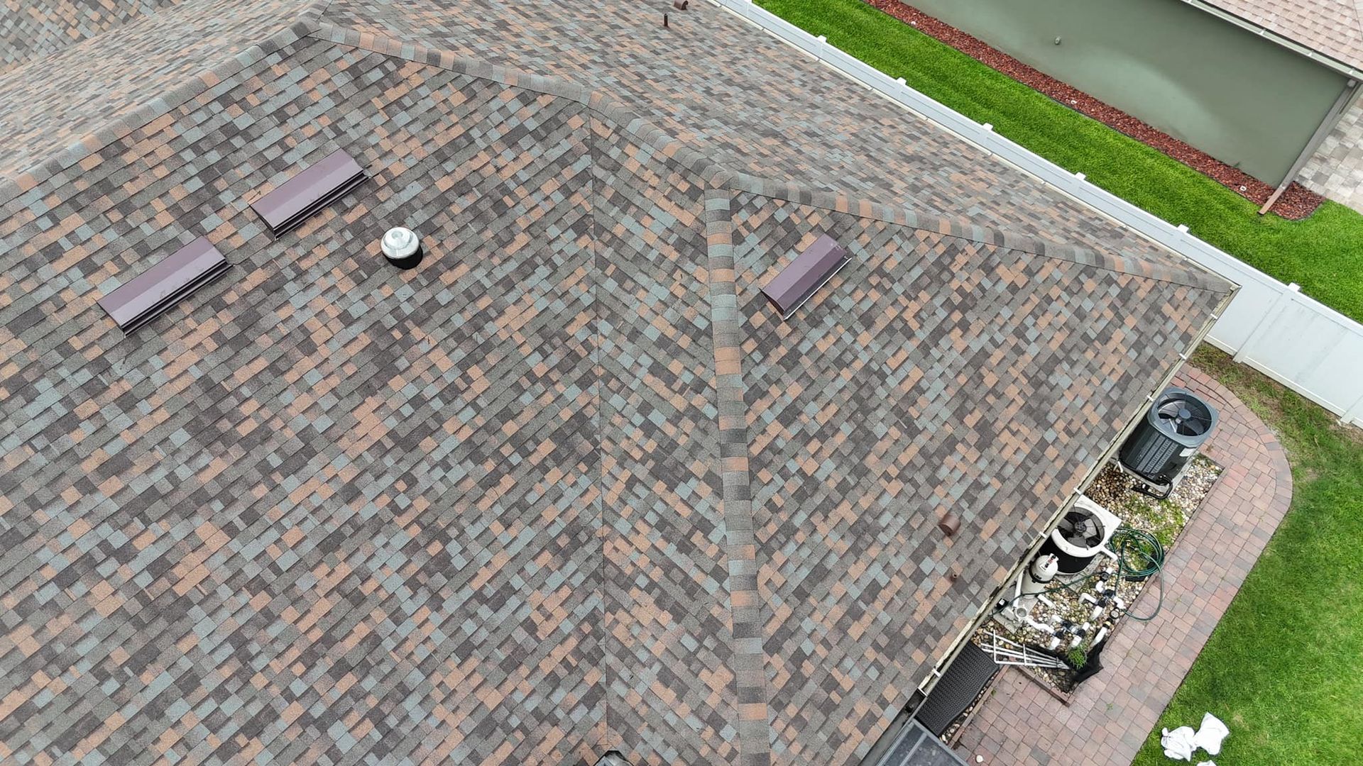 An aerial view of a textured, multi-colored shingle roof with three rectangular vents and a circular pipe flashing.
