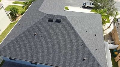 An aerial view of a dark grey shingled roof on a residential house in a suburban neighborhood.