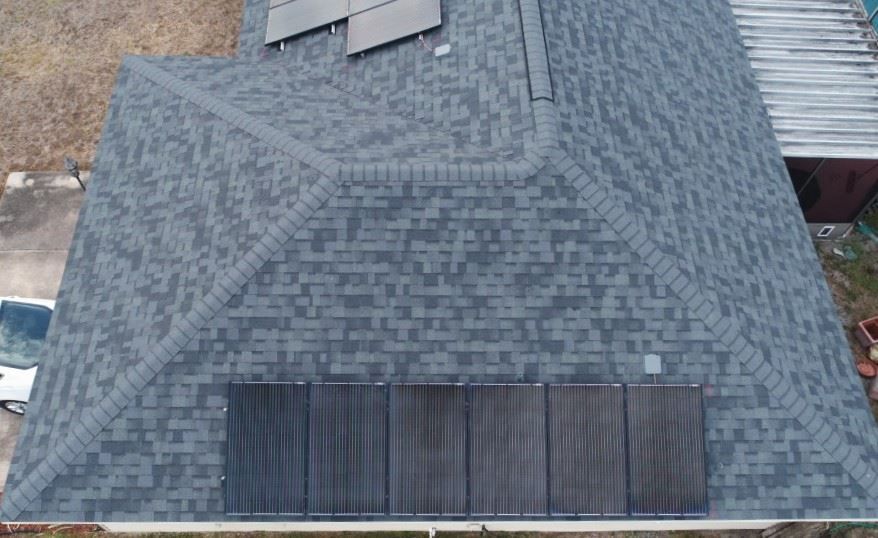 An aerial view of a dark grey shingled roof with two sets of solar panels installed on different slopes.