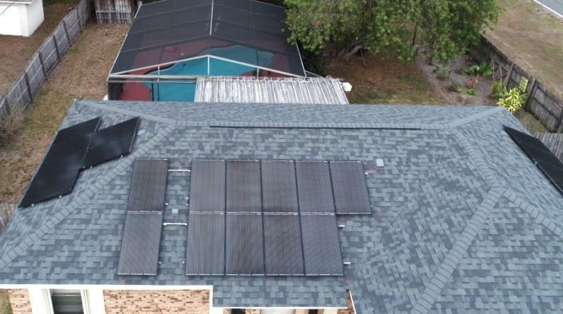 Aerial view of a residential shingled roof featuring a solar panel array and a separate pool heating collector.