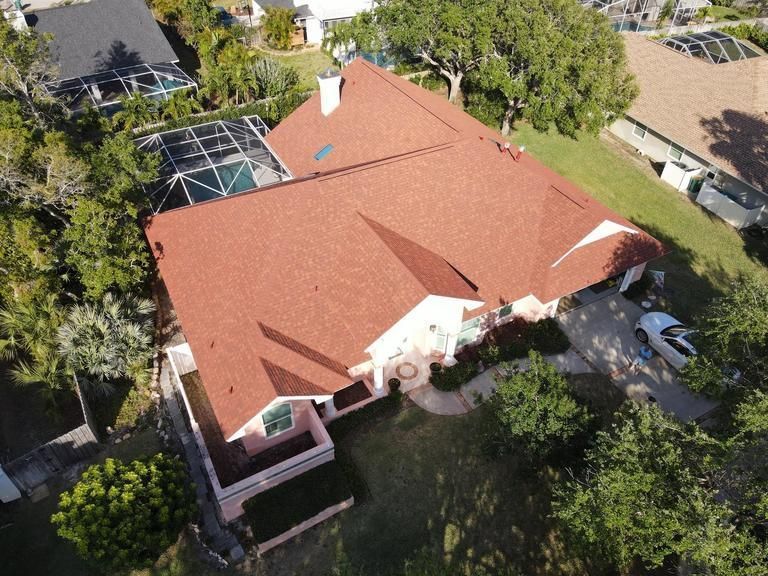 An aerial view of a single-story house with a red roof, a screen-enclosed pool, and a driveway with a car.