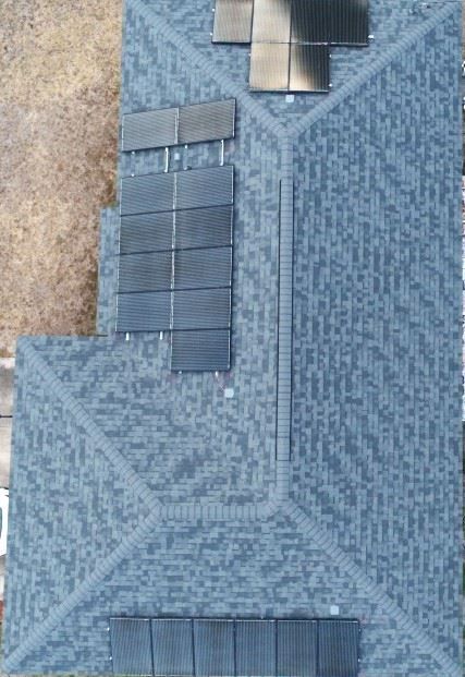 An aerial view of a dark grey shingled roof with several solar panels installed in two distinct sections.