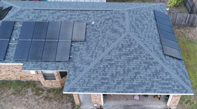 An overhead view of a residential shingled roof featuring a large solar panel array on the left and a smaller one on right.