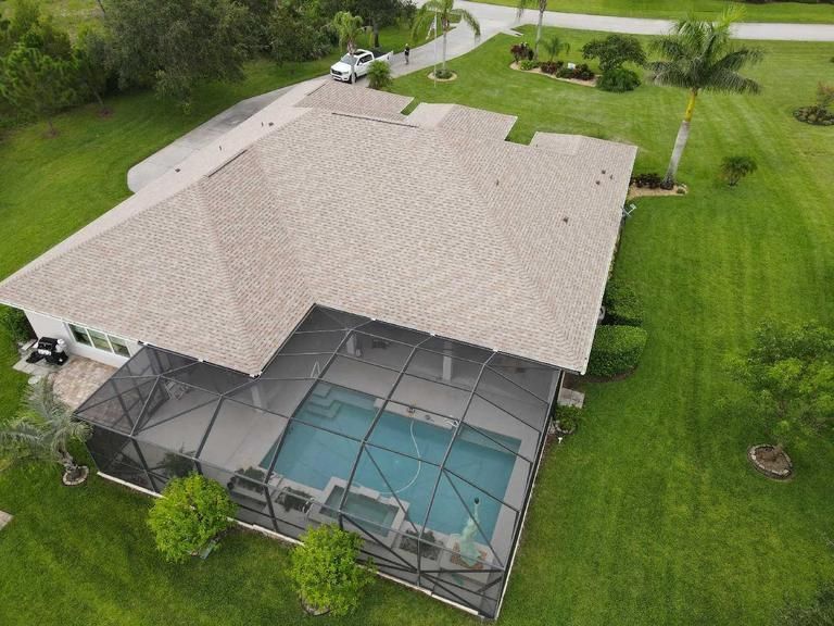 Aerial view of a suburban house with a screened-in swimming pool in the backyard surrounded by a green lawn.