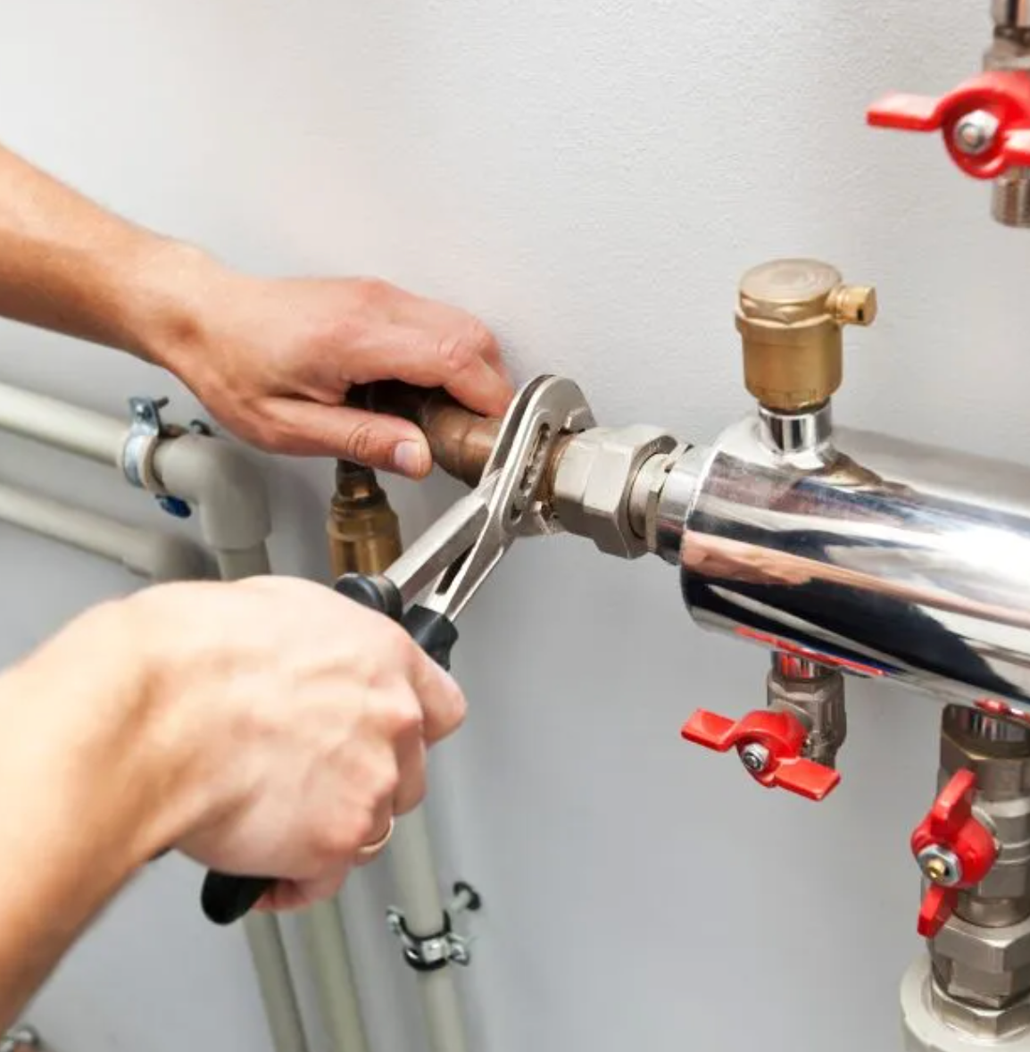 Licensed plumber tightening indoor pipes with a wrench, ensuring high-quality plumbing work.