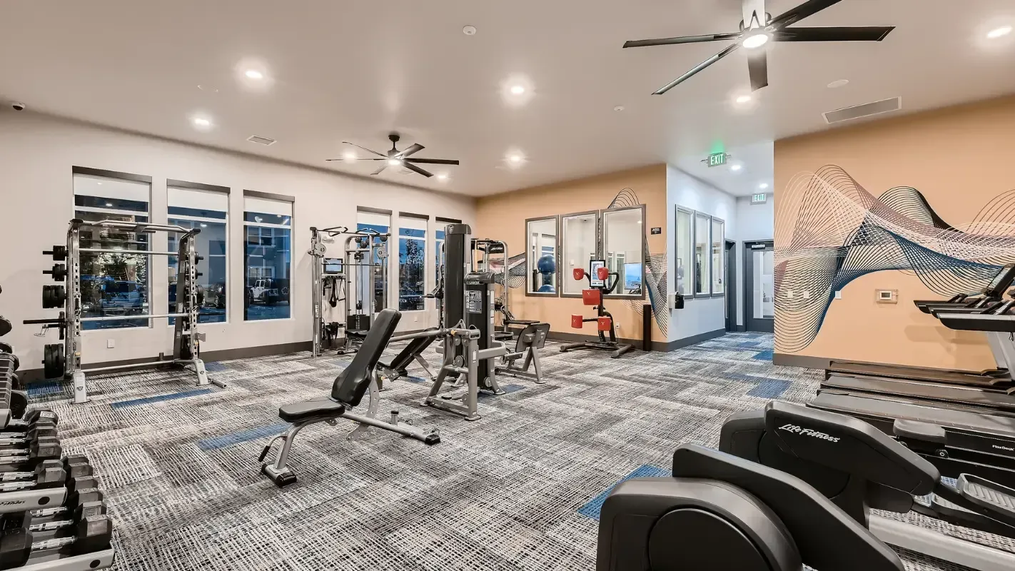 Interior community gym with free weights, strength machines, and cardio equipment.