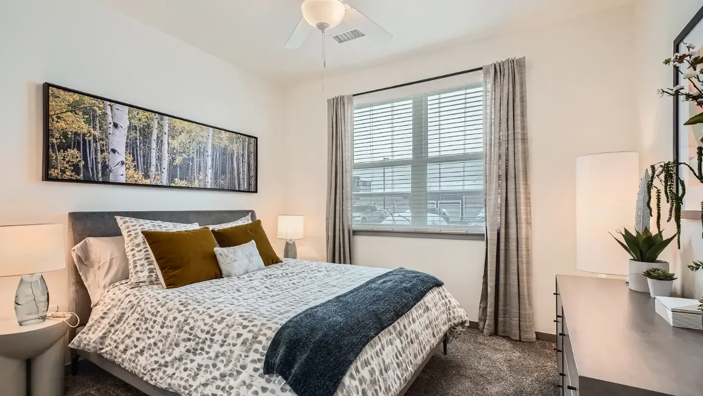 Bedroom in a modern apartment with a queen bed, nightstands, dresser, and a large window.