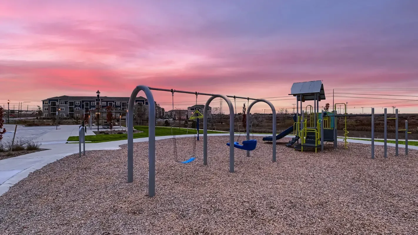 Sunset over a playground at a multifamily community with swings and a slide.