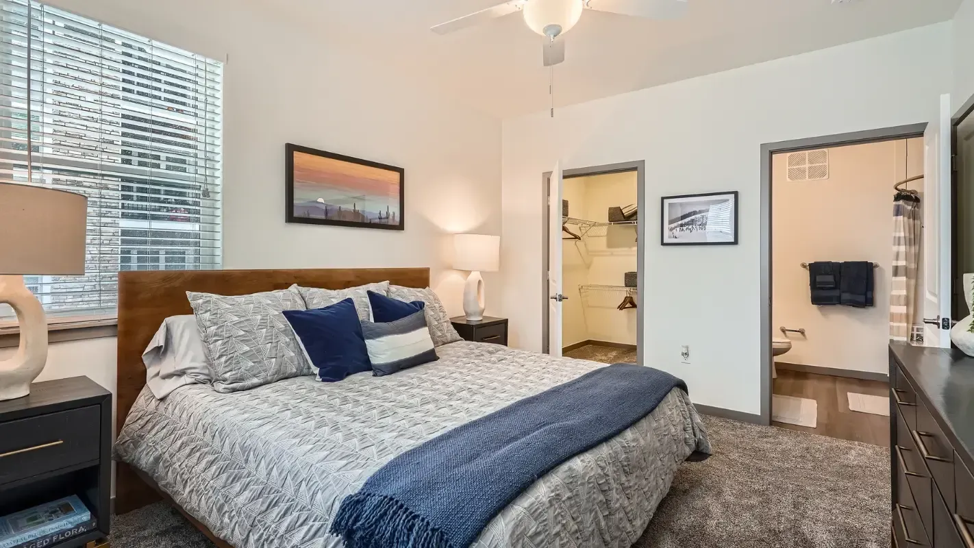 Bright apartment bedroom with queen bed, two nightstands, dresser, and an open closet.