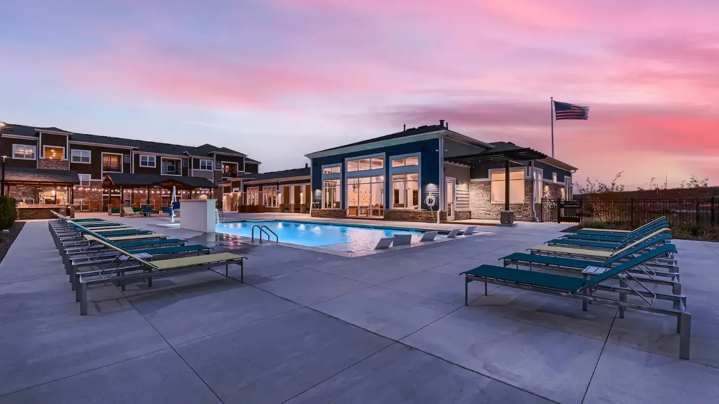 Outdoor community pool area with lounge chairs and a modern clubhouse at sunset.