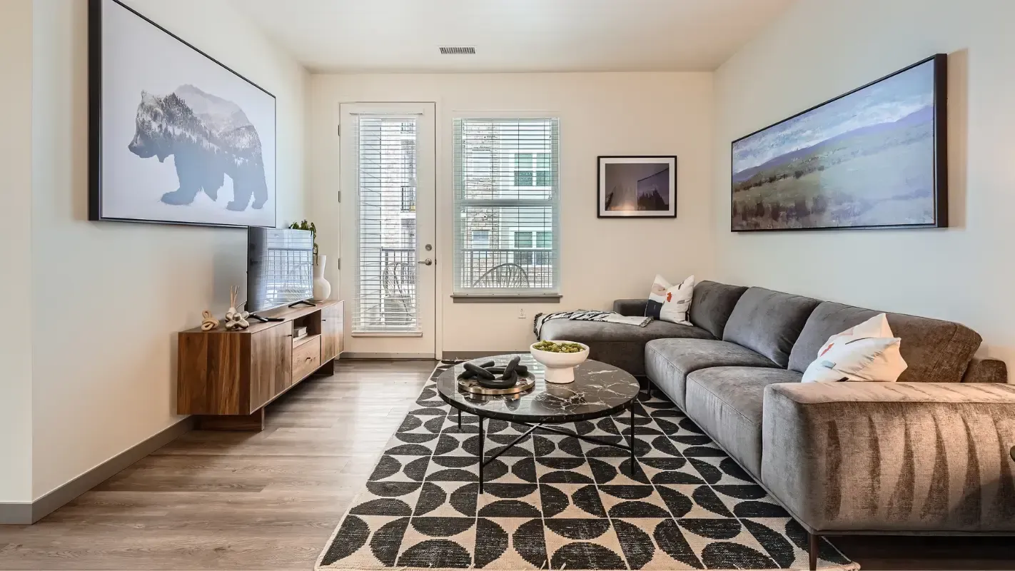 Living room with a gray sectional, round marble coffee table, TV console, and large windows.