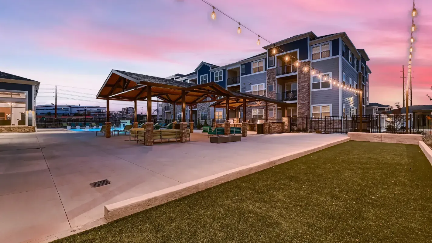 Exterior communal pool area with a pavilion, string lights, and lounge seating at dusk.