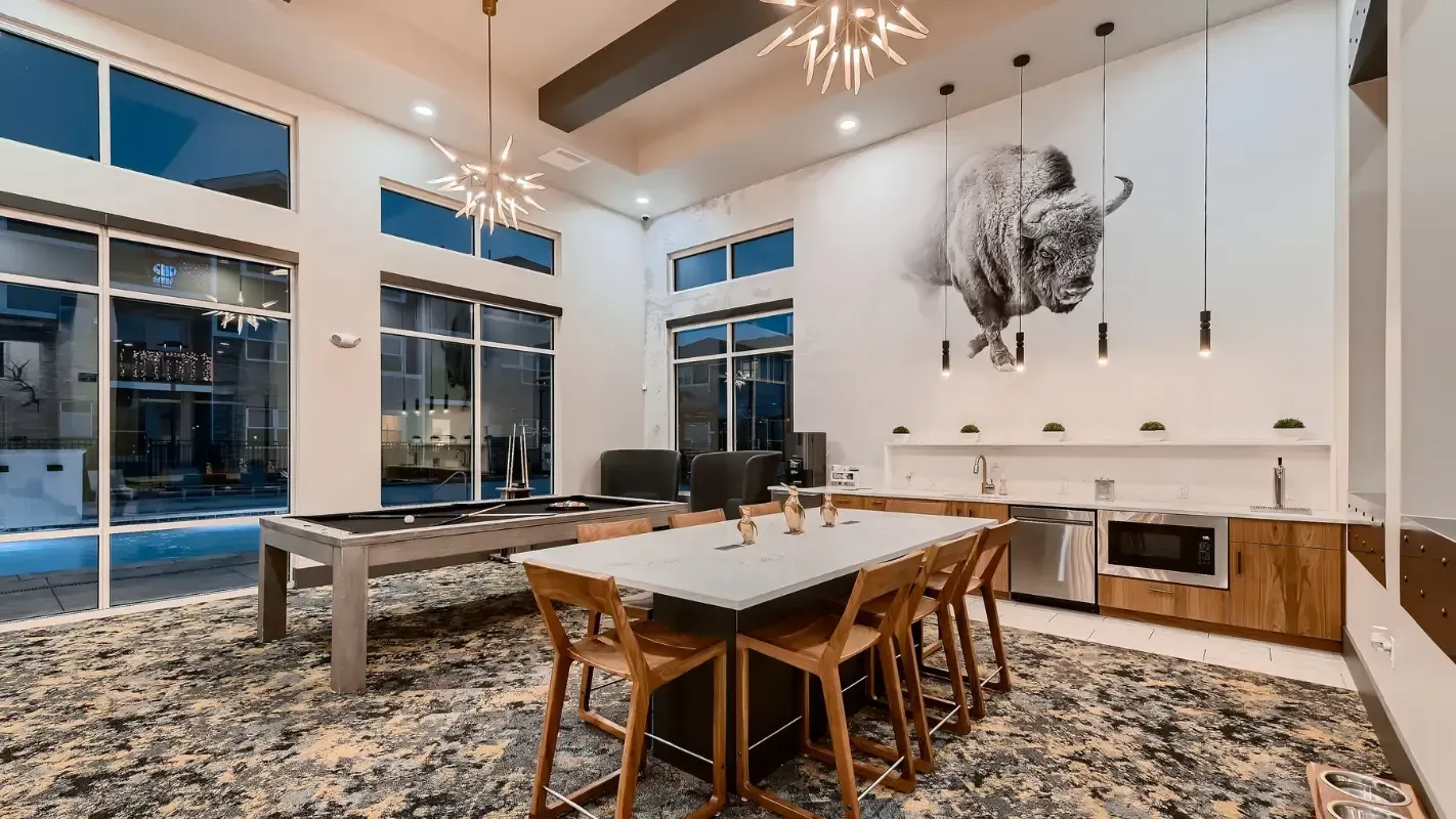 Interior community lounge with a long dining table, pool table, and kitchenette; buffalo mural on the wall.