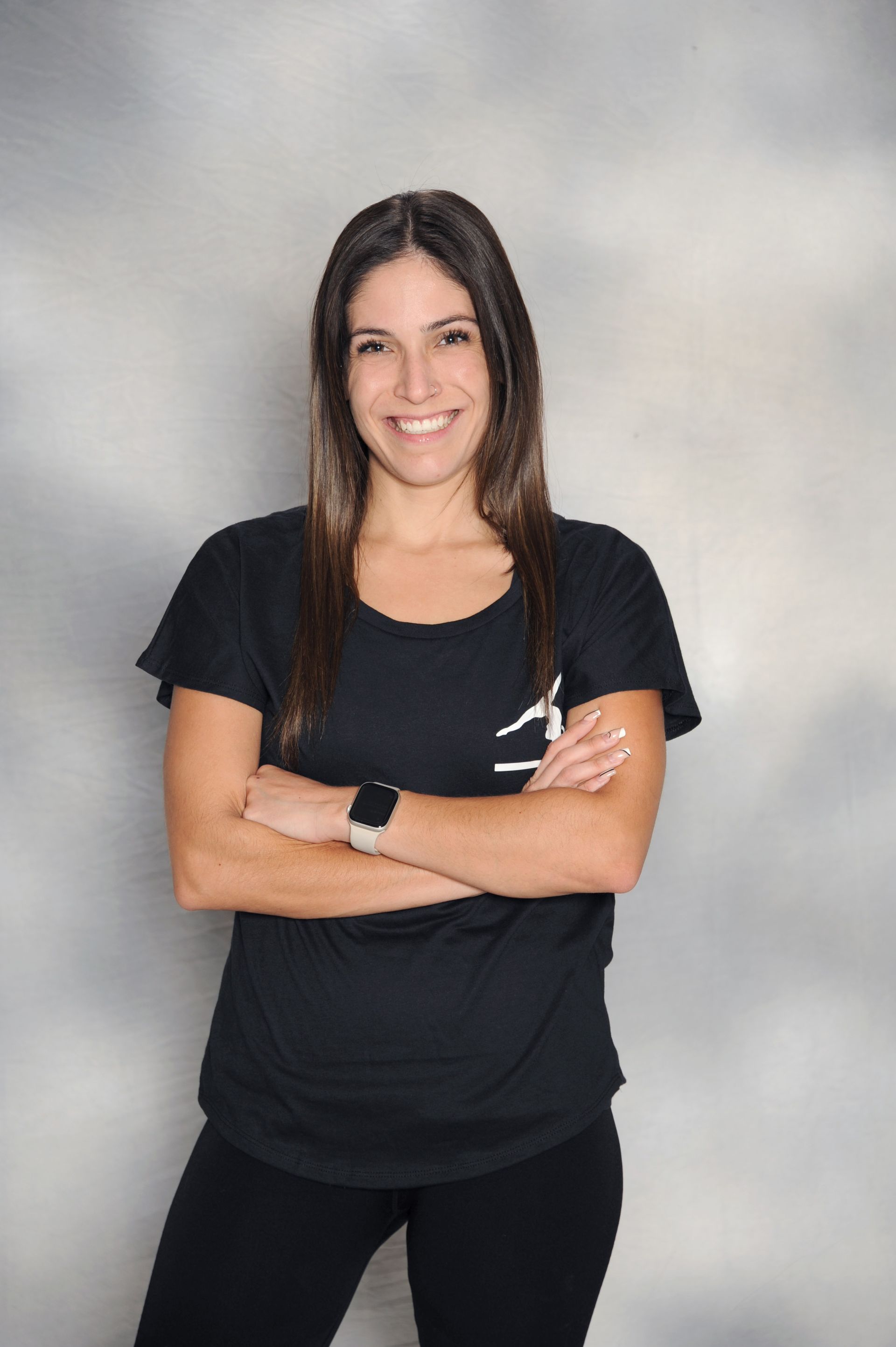 A woman in a black shirt is standing with her arms crossed and smiling.