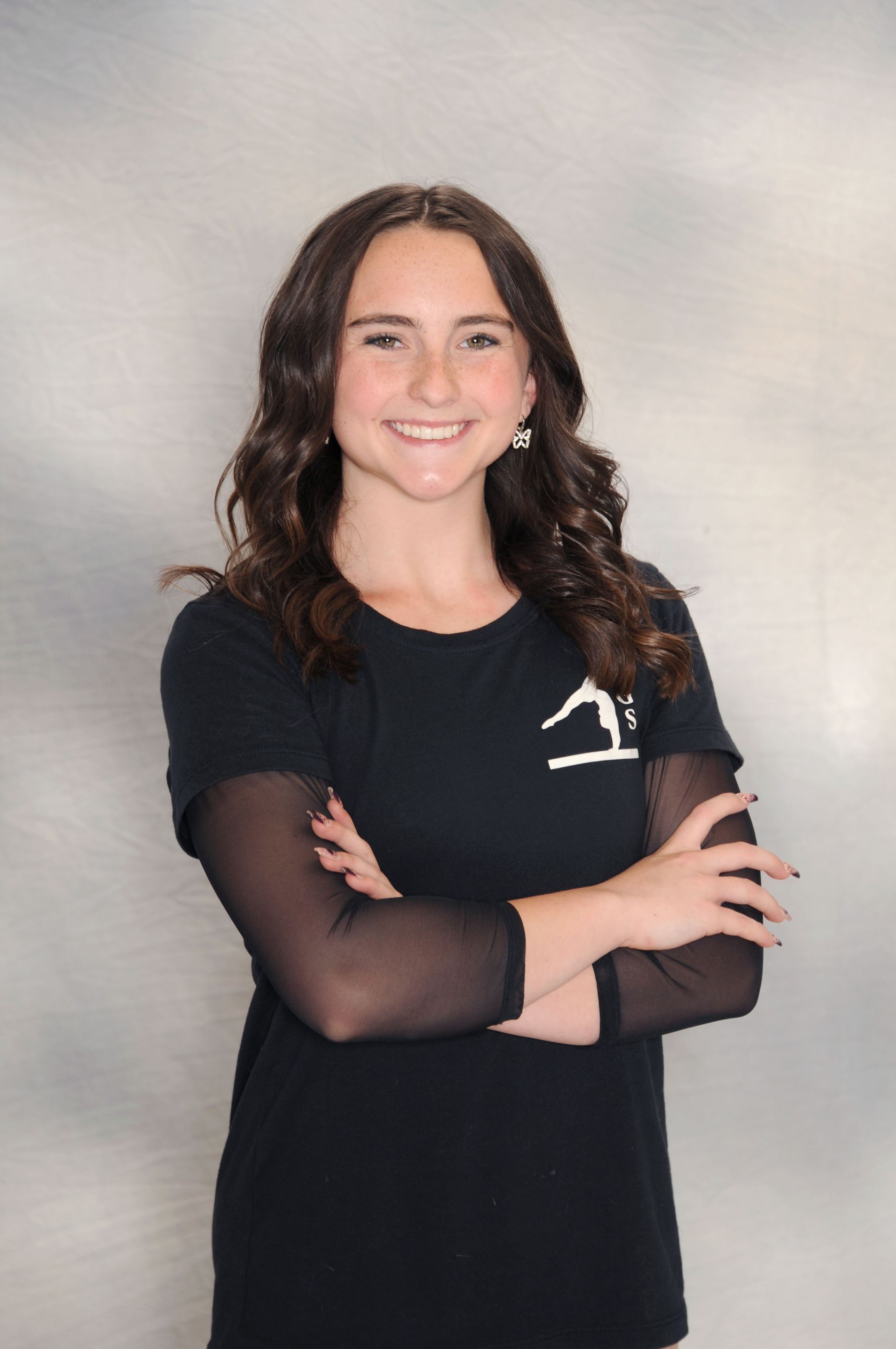 A woman wearing a black shirt with the letter g on it is standing with her arms crossed.