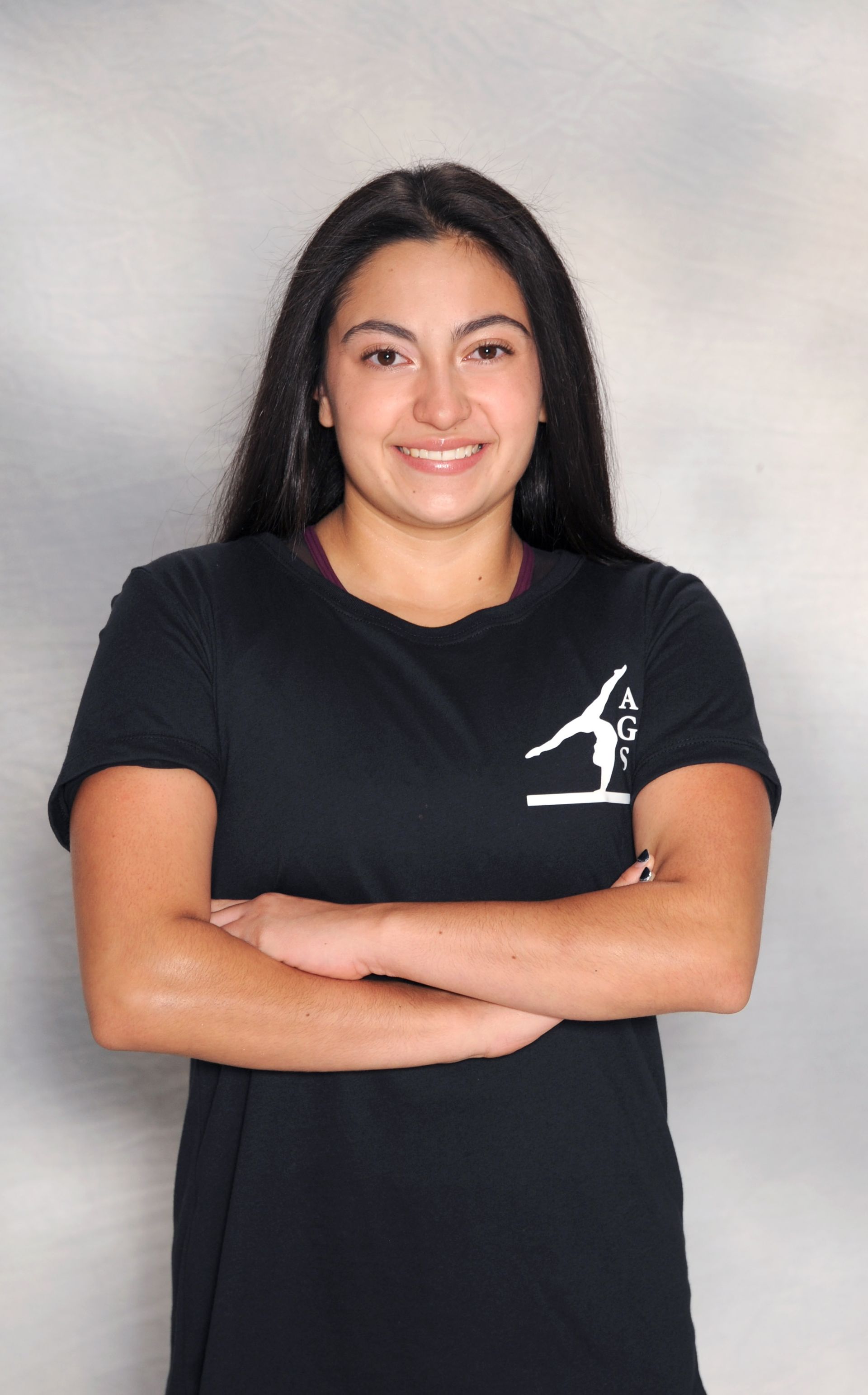 A woman wearing a black shirt with a gymnast on it is standing with her arms crossed.