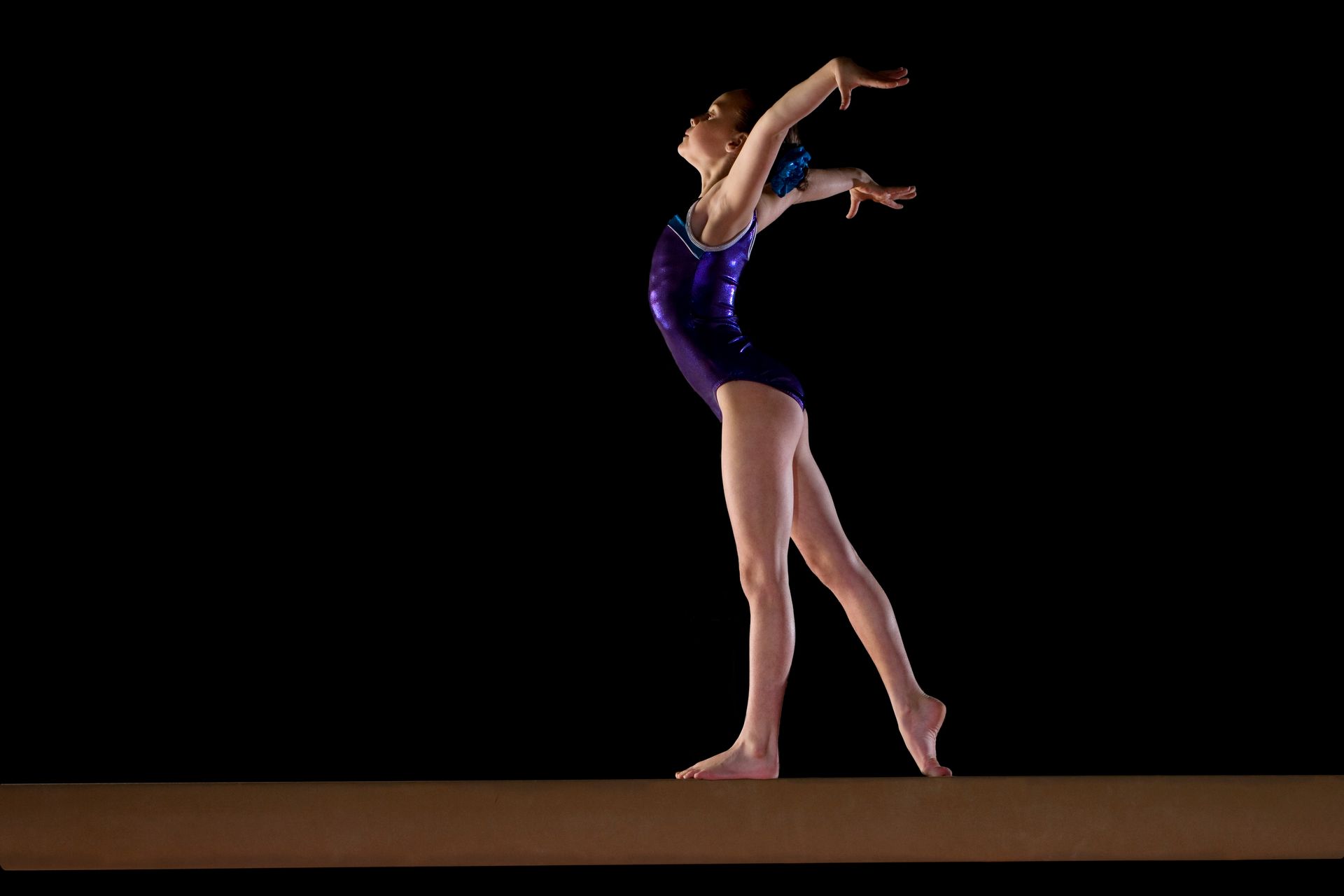 A female gymnast is doing a handstand on a balance beam.