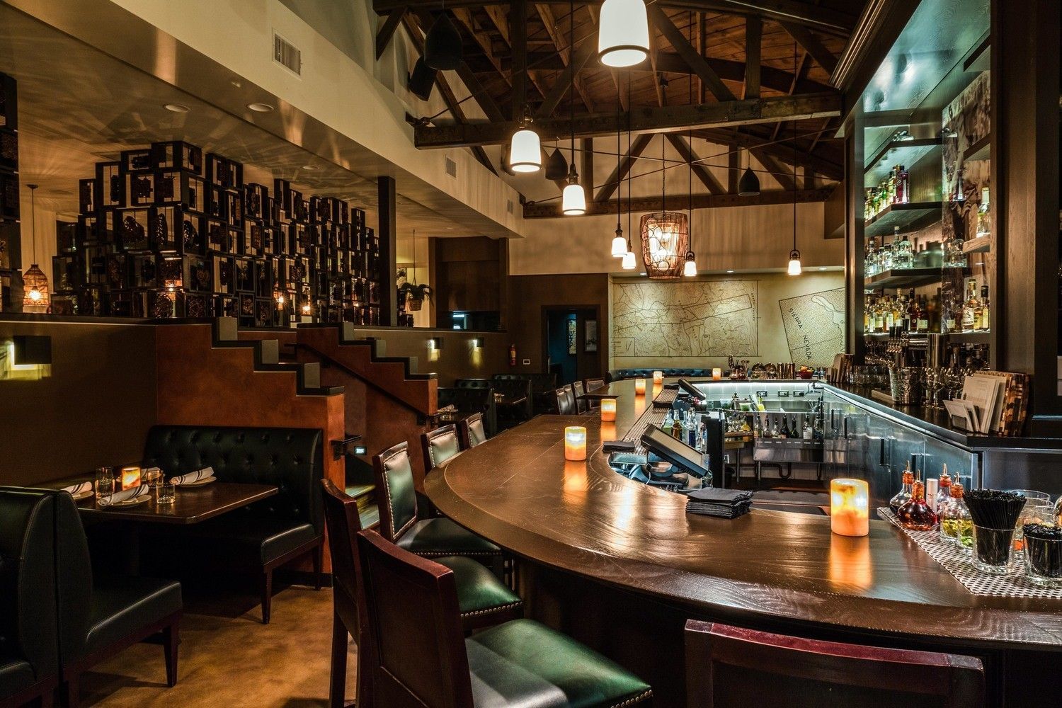 Interior of a dimly lit restaurant, featuring a bar with stools, tables, and wooden beams.