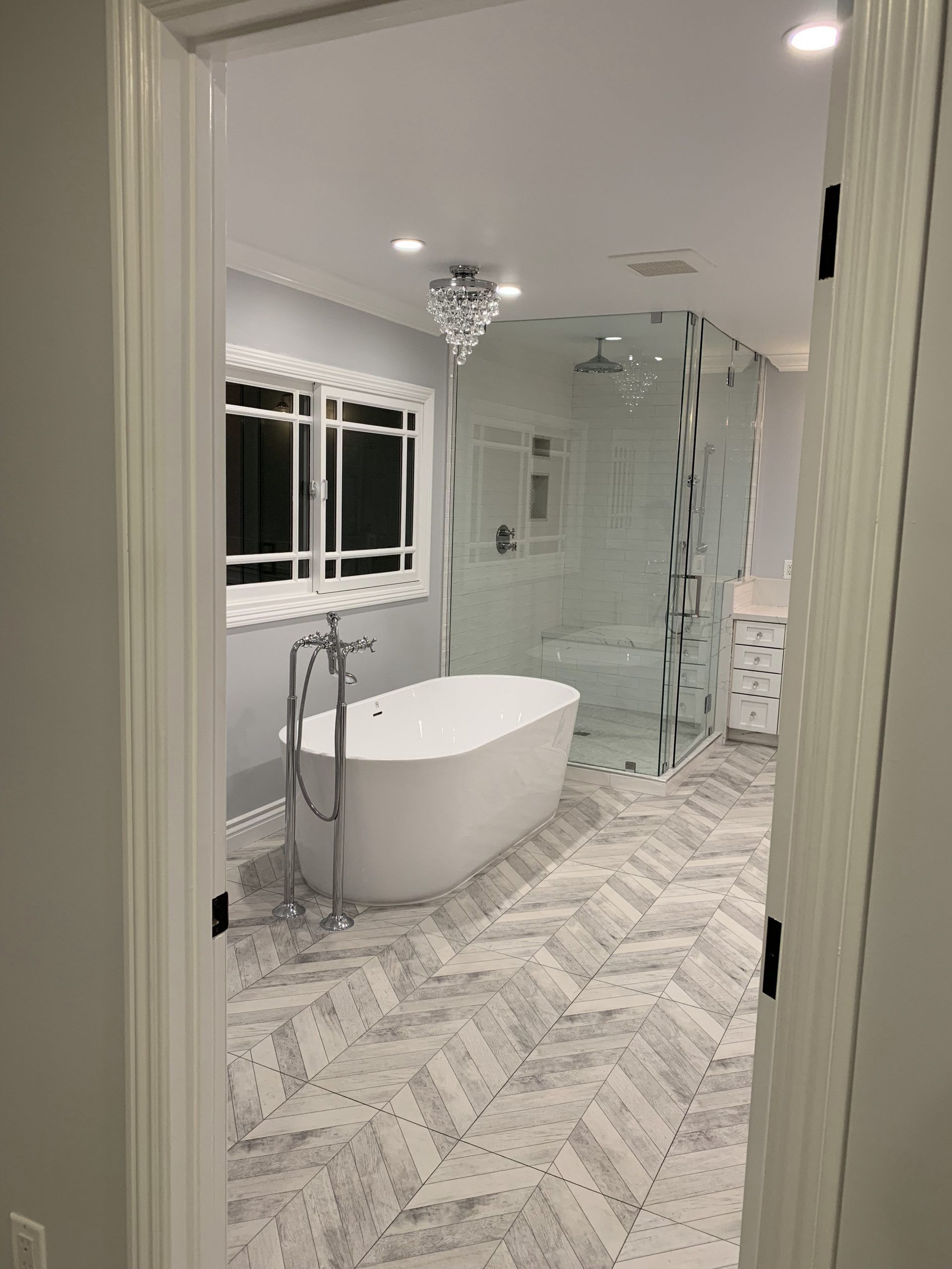 A luxurious bathroom with a freestanding tub, glass shower, and herringbone tile flooring.