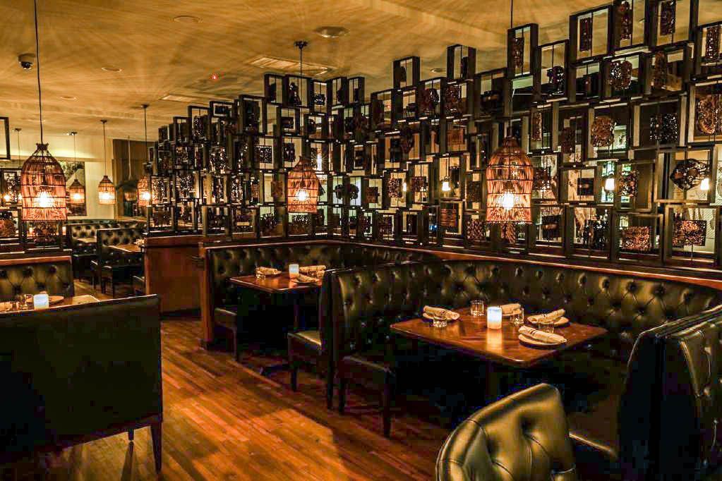 Restaurant interior with dark leather booths, wooden tables, framed wall decor, and ambient lighting.