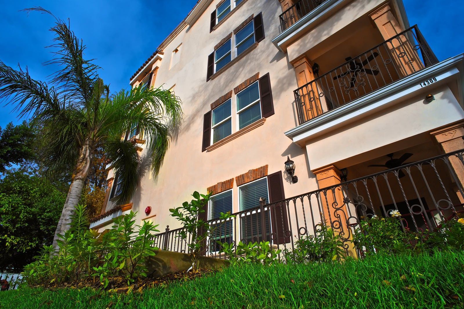 Apartment building exterior with peach-colored walls, brown shutters, and wrought-iron balconies under a blue sky.