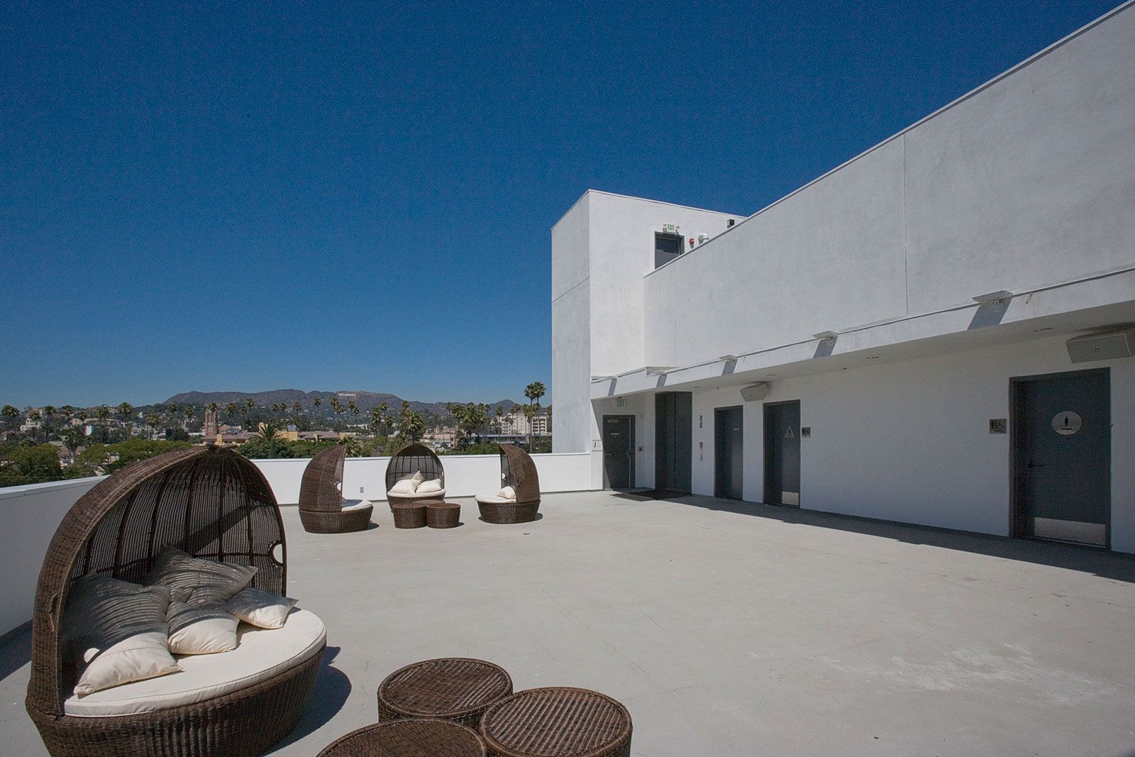 Rooftop patio with lounge furniture, clear blue sky. Hollywood sign visible in the distance.