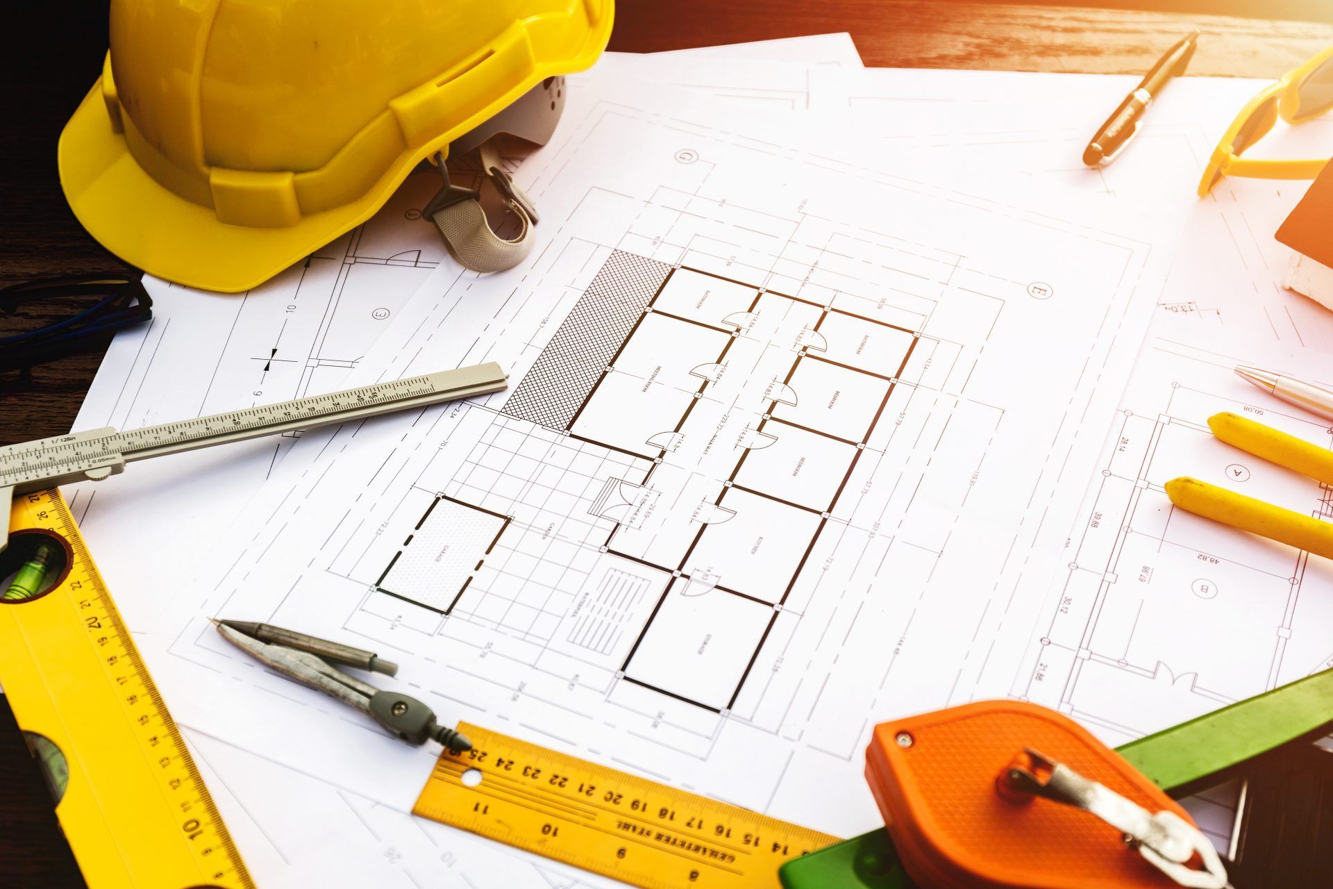 Blueprint surrounded by tools, yellow hard hat, and drafting supplies, representing construction planning.