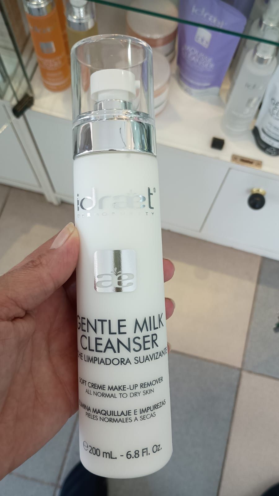 Una mano sostiene un frasco blanco de Hidradet Gentle Milk Cleanser en un entorno de tienda