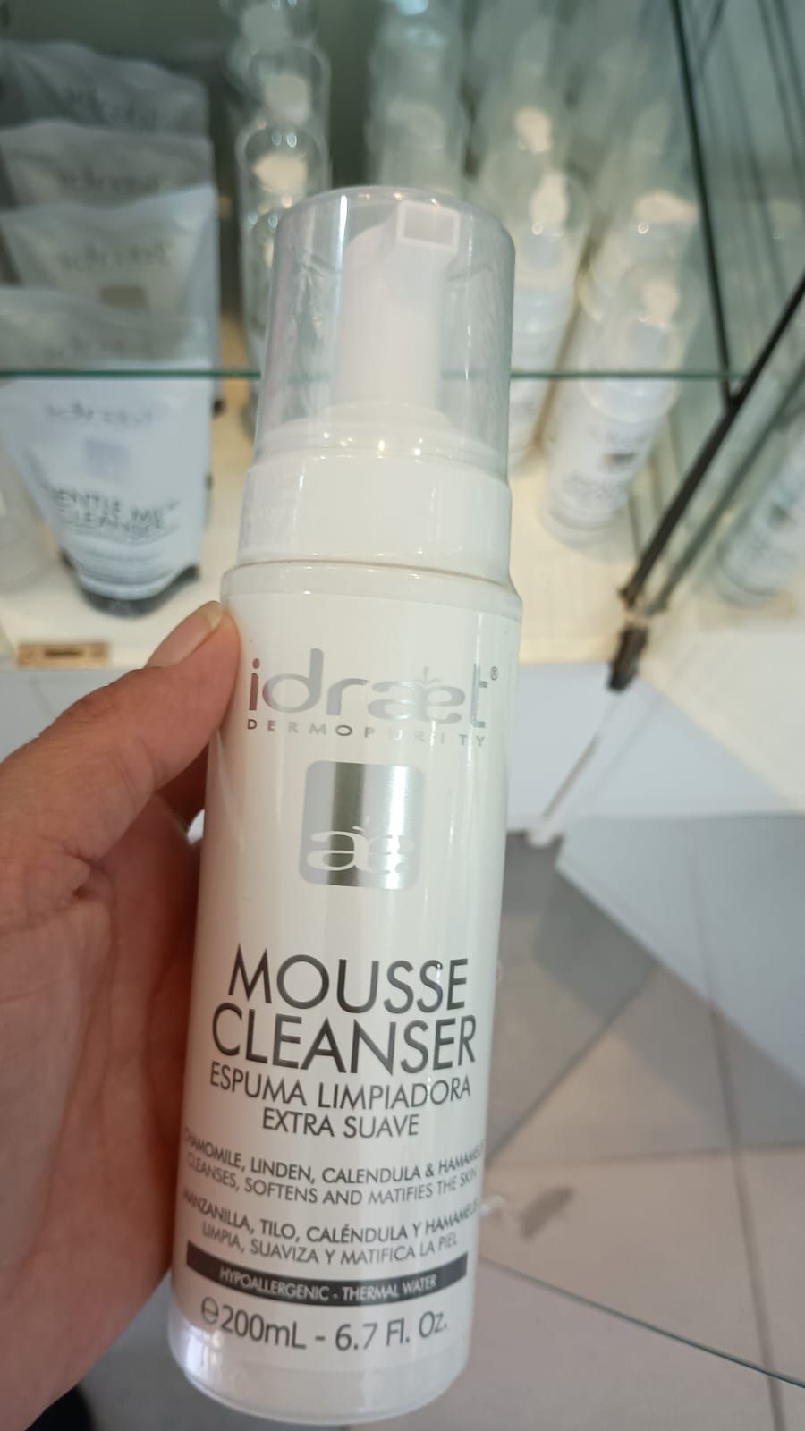 Una mano sostiene una botella blanca de limpiador facial en mousse Idraet
