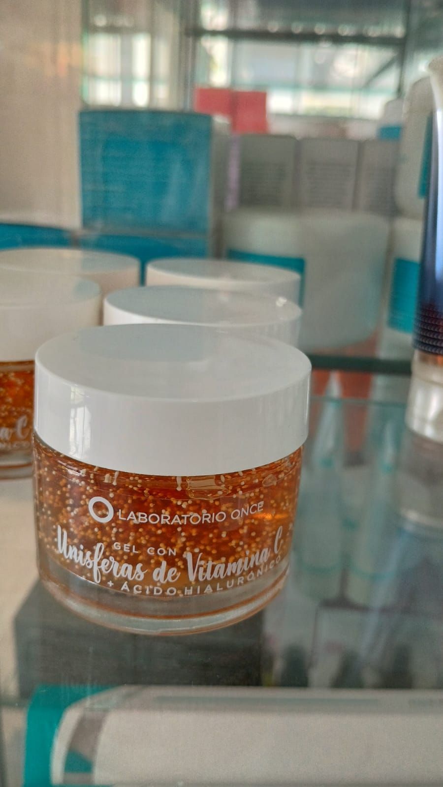 Un frasco de gel de perlas de vitamina E de color naranja sobre un estante de vidrio en una tienda.
