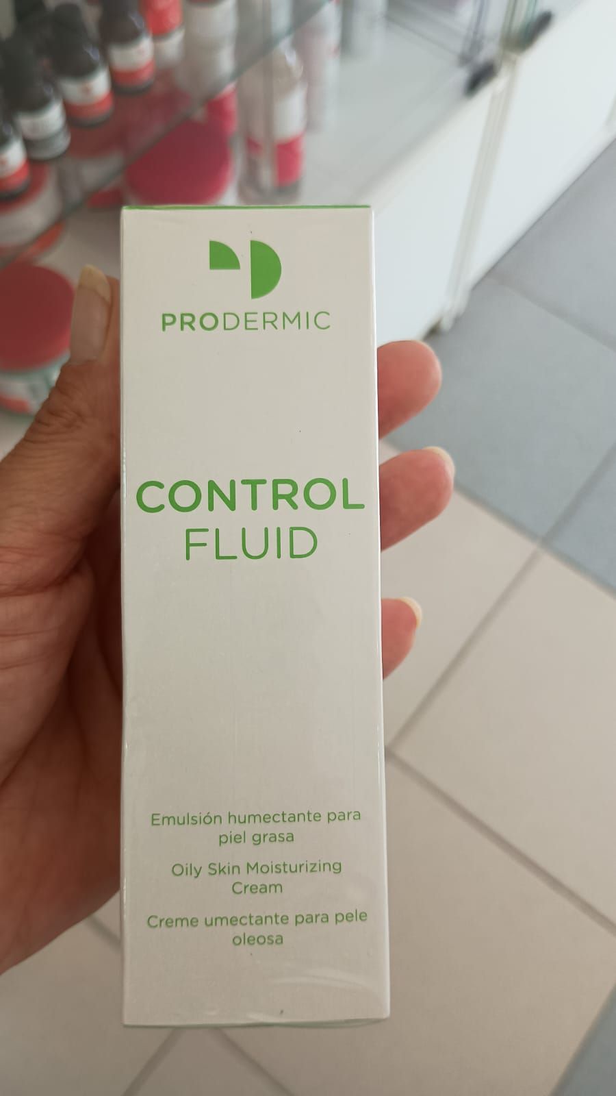 Una persona sostiene una caja rectangular blanca de Prodermic Control Fluid para piel grasa sobre un fondo borroso.