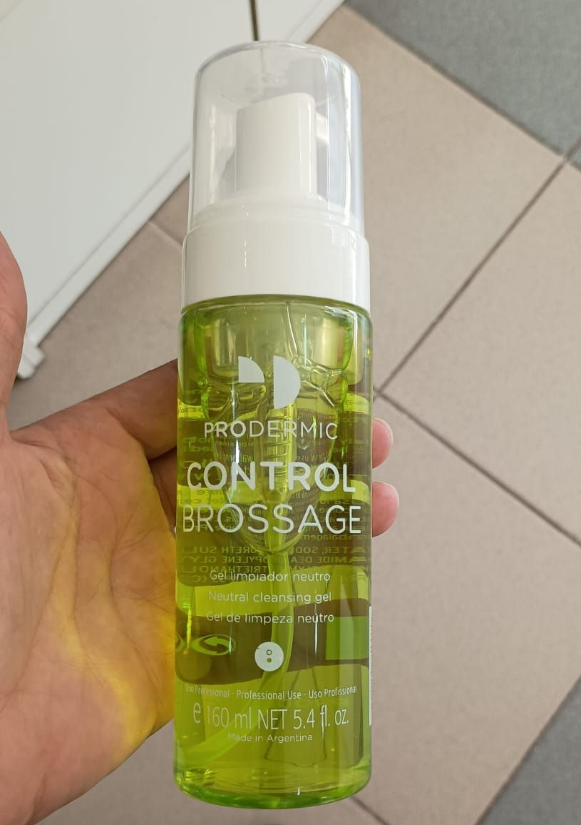 Una mano sostiene un frasco transparente de limpiador facial en espuma PRODERMIG 