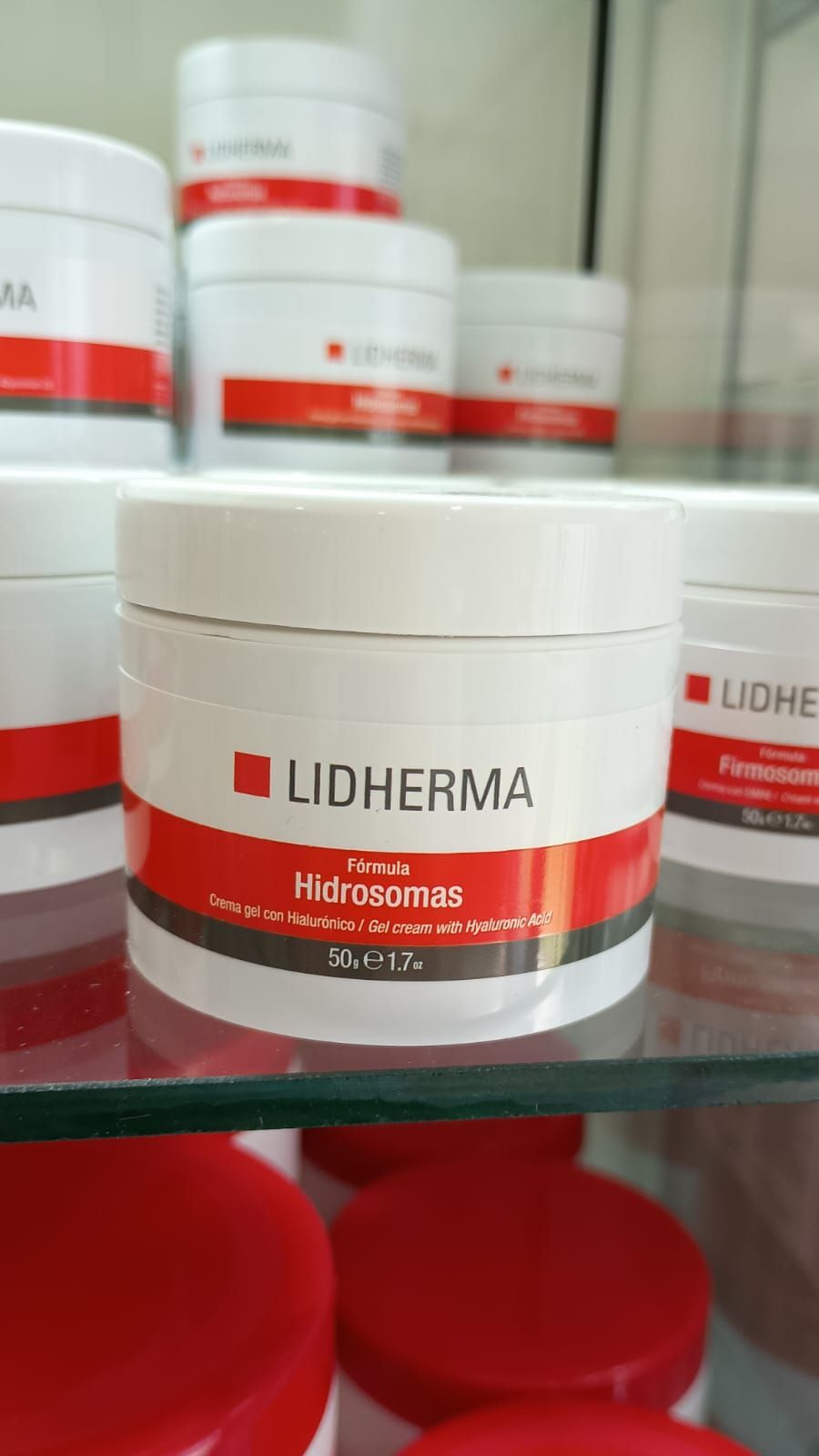 Un tarro blanco de Lidherma Hidrocrem con el logotipo en rojo y negro, colocado en una estantería de cristal