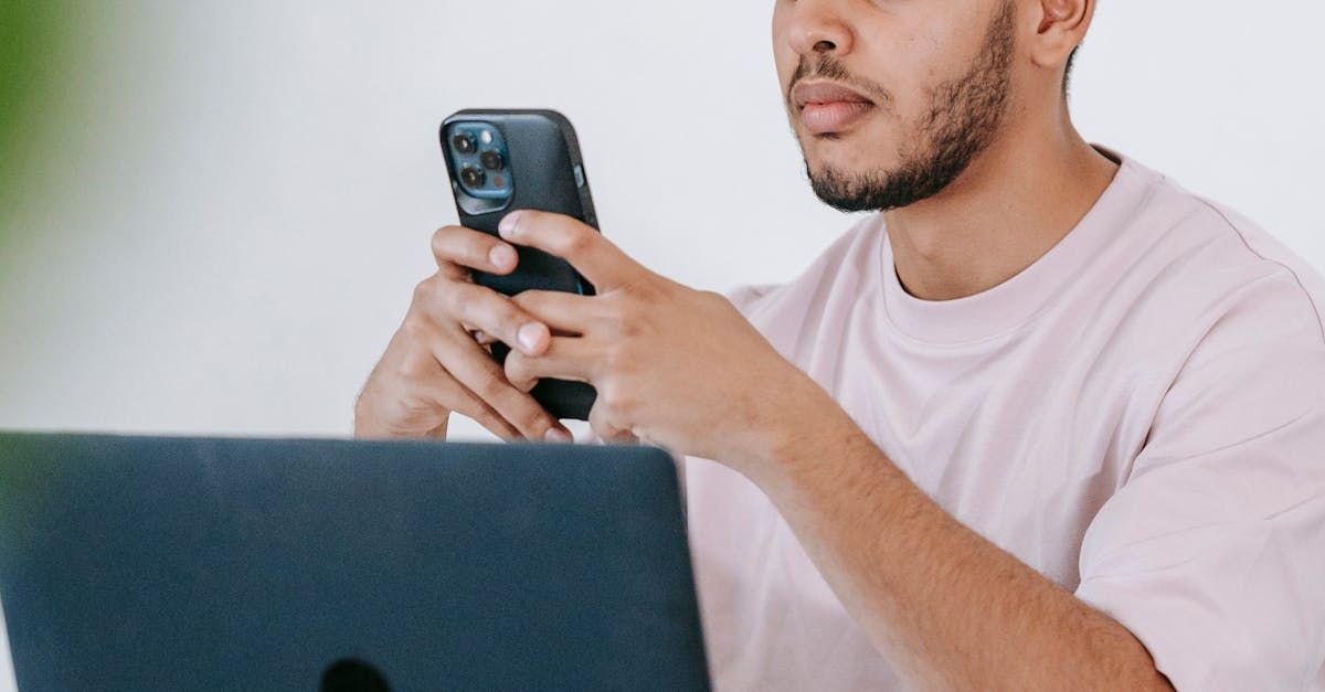 A younger man holding a cell phone while working on a computer.