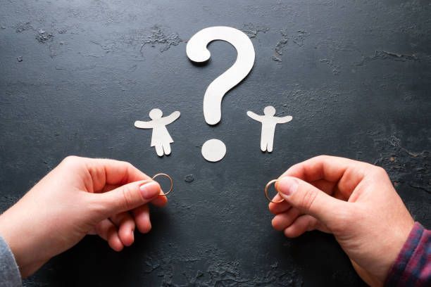 A person is holding a pair of wedding rings in front of a question mark.