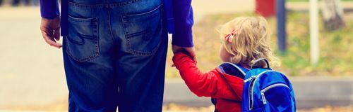 A man is holding the hand of a little girl with a backpack.