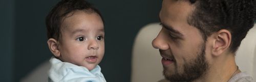 A man is holding a baby in his arms and looking at it.