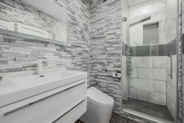 Modern bathroom with white vanity, toilet, and textured gray and white tiled walls and shower.